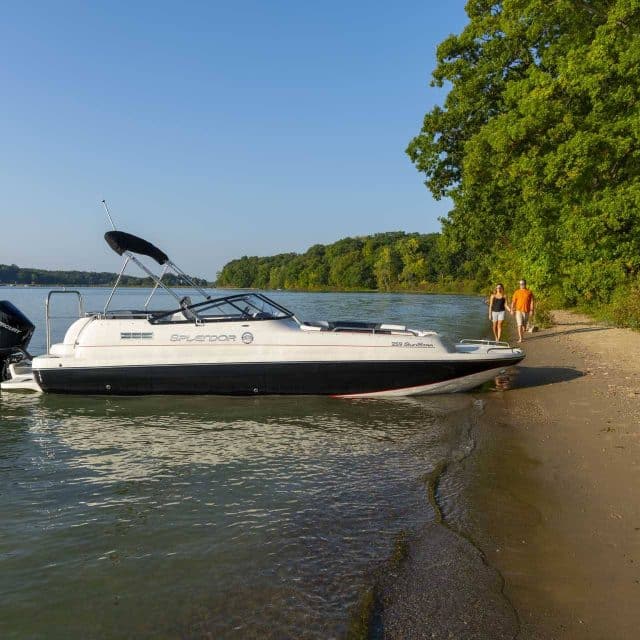 A Splendor deck boat parked in shallow water against a sandy beach.