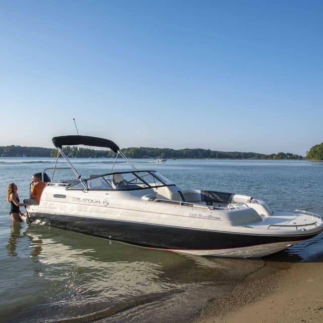 One of Splendor Boats' customized deck boats docked at a sandy beach with people sitting on the back.