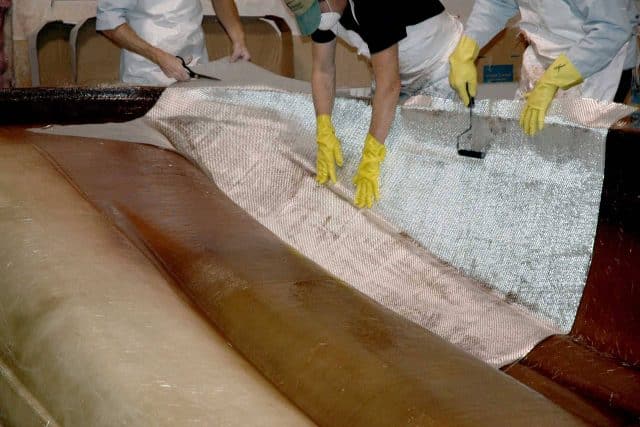 Three sets of hands wearing yellow rubber gloves working with the fabric necessary for Splendor Boats' deck boat construction process.