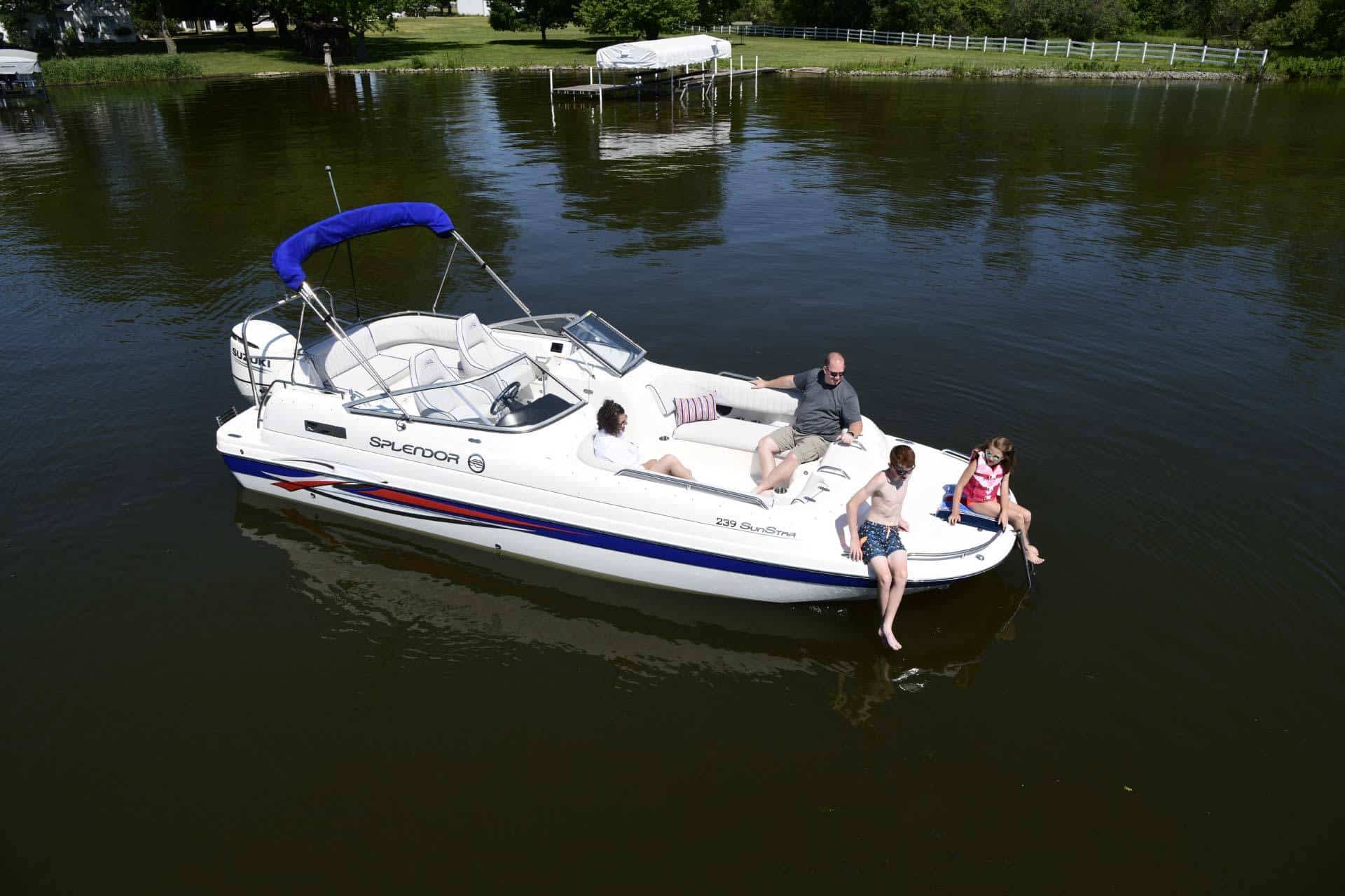 A white Splendor catamaran boat sitting in a lake with two adults and two children sitting in it.